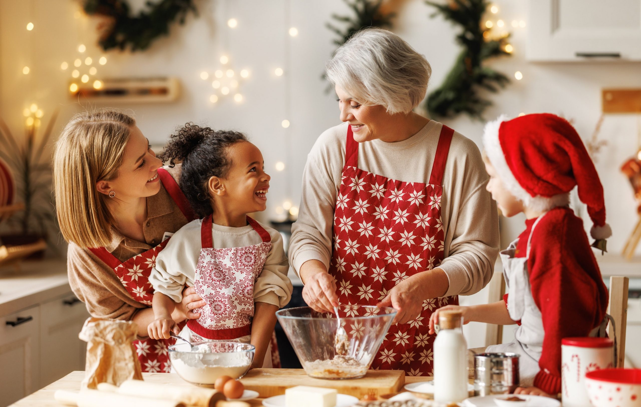 Older woman baking in the kitchen of a foster home. The foster mom and foster children are smiling while watching her work.