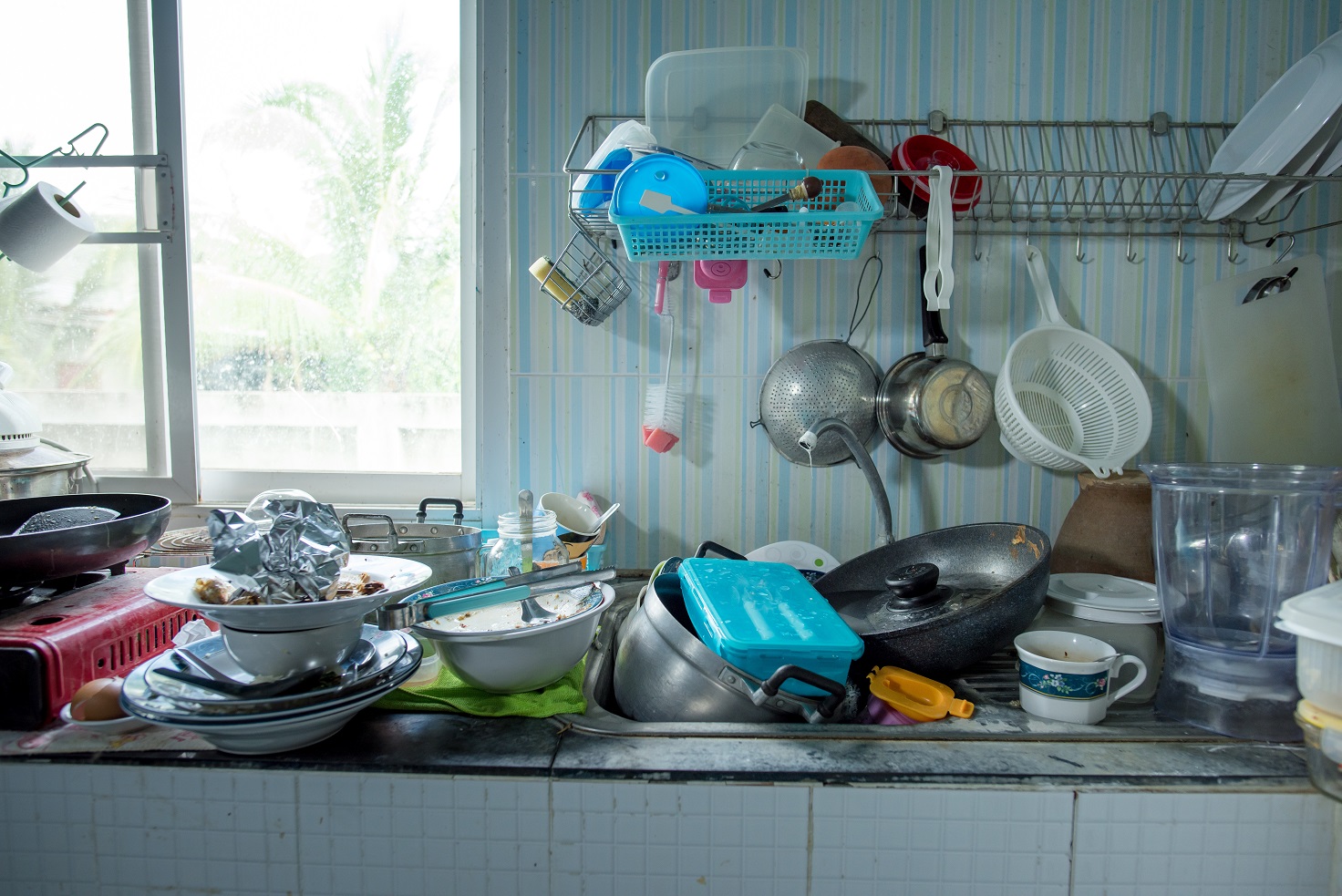 Image of a dirty kitchen with used utensils and food containers all over the counter.